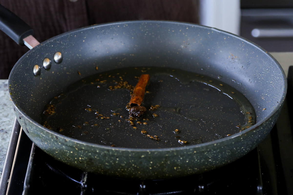 adding more whole spices to the toasted cumin seeds in the pan