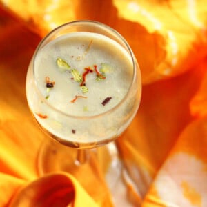 An overhead shot of a glass of thandai on an orange fabric background