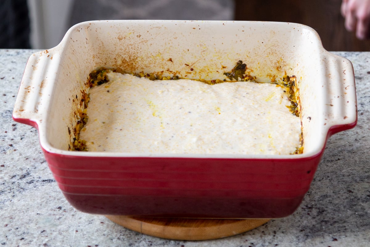 cornbread topping being spread on greens in a red casserole dish 