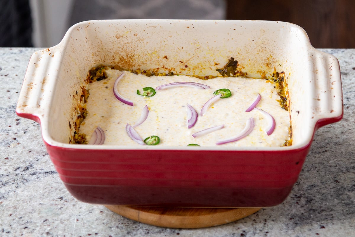 saag casserole topped with cornbread topping, sliced onions and chilies