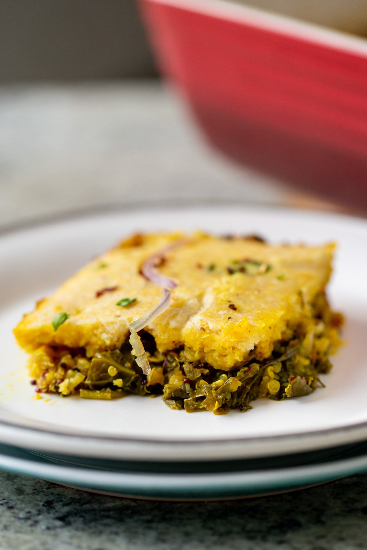 a slice of saag casserole topped with cornbread topping on two stacked white plates