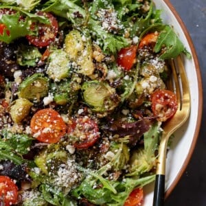 close-up of shaved Brussels sprouts salad in a bowl with tomatoes, lettuce, and walnut crumble