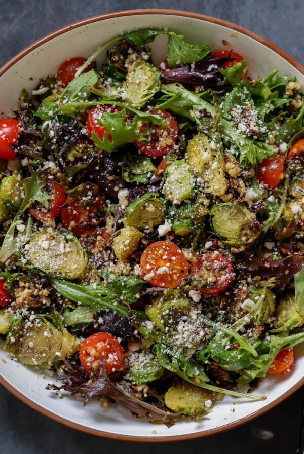 shaved Brussels sprouts salad in a bowl with tomatoes, lettuce, and walnut crumble