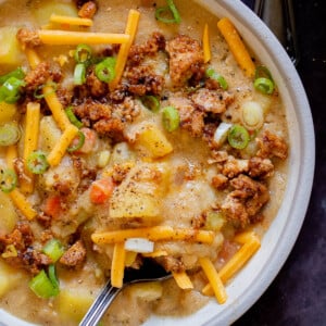 bowl of smoky vegan potato soup topped with tofu crumbles, green onions, and vegan cheese