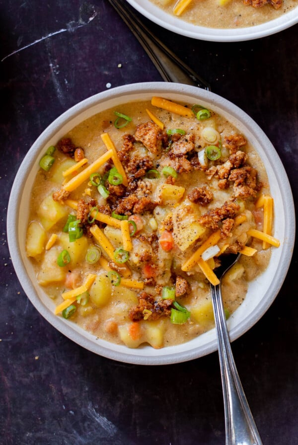 bowl of smoky vegan potato soup topped with tofu crumbles, green onions, and vegan cheese