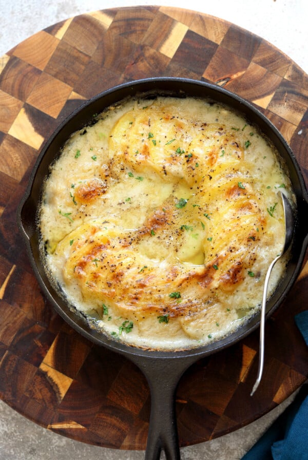 Vegan Scalloped Potatoes in a cast iron skillet on wood board