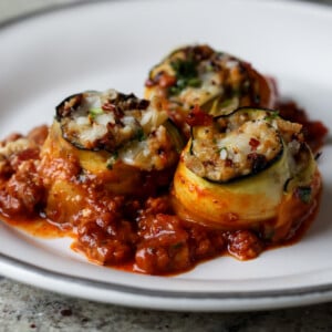 zucchini rolls on a white plate with tomato sauce